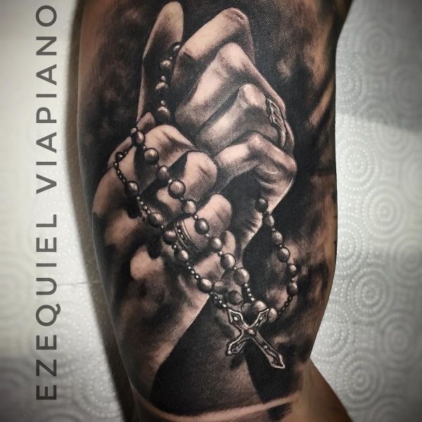 Des mains en prière comme tatouage sur le biceps d'un homme.